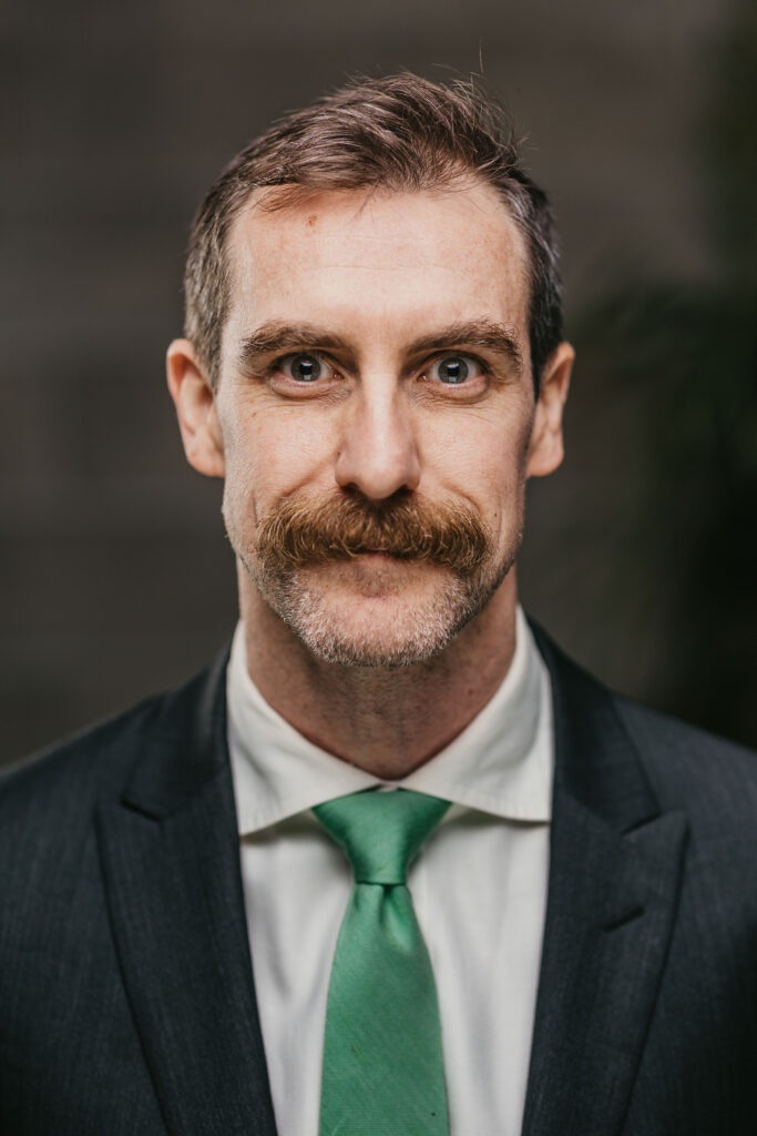A man with a mustache and green tie, Stephen Glanzberg, at a charity event at Clark Woods LLP